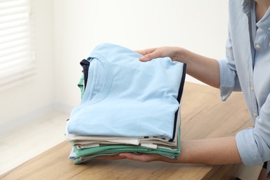 Photo of Woman stacking clean clothes at wooden table indoors, closeup