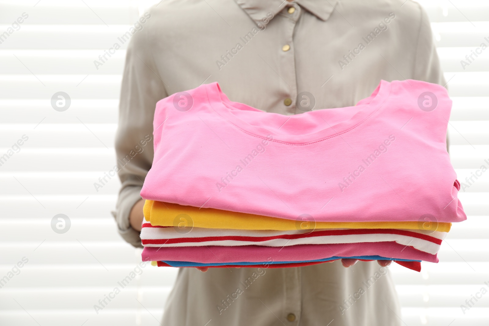 Photo of Woman with stack of clean clothes indoors, closeup