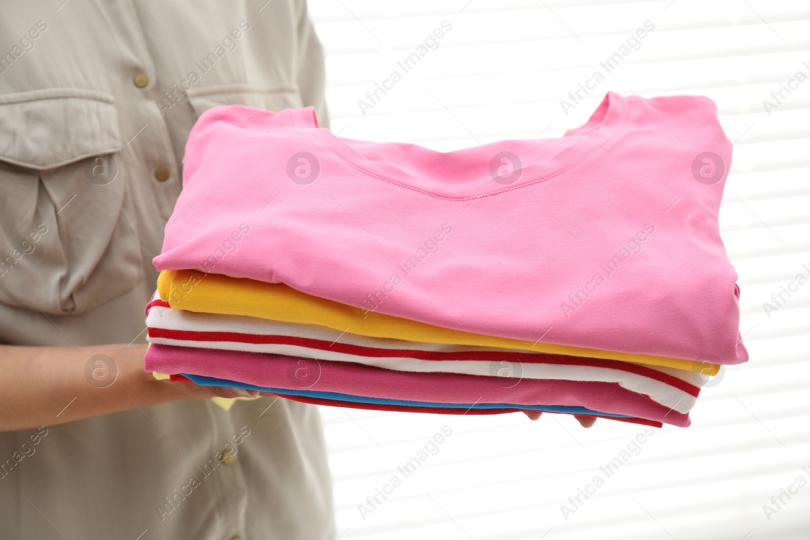 Photo of Woman with stack of clean clothes indoors, closeup