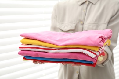 Photo of Woman with stack of clean clothes indoors, closeup