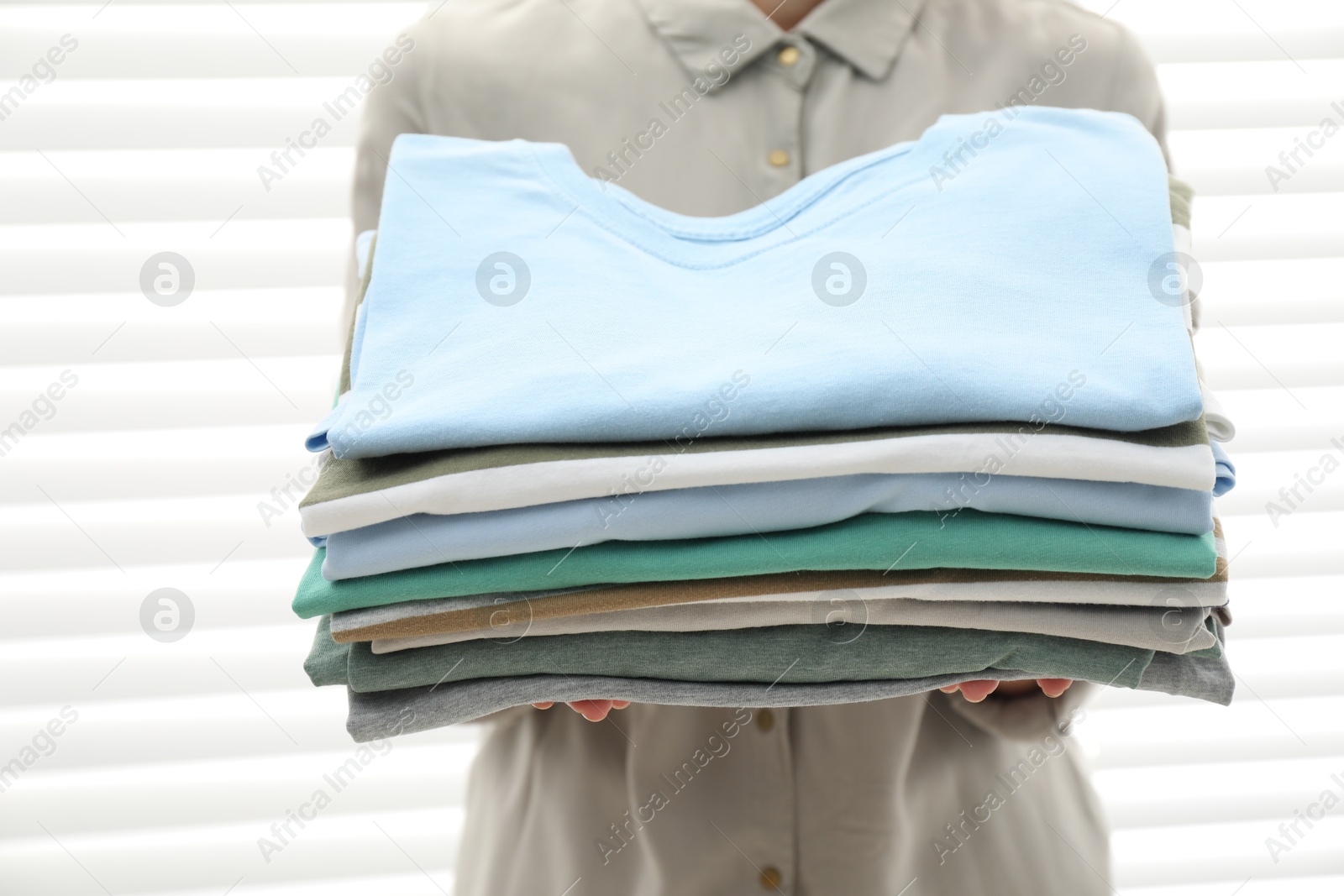 Photo of Woman with stack of clean clothes indoors, closeup