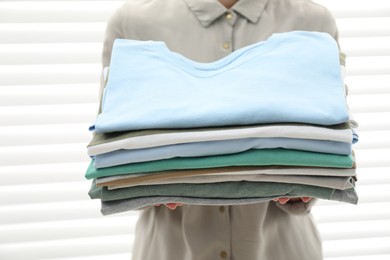 Woman with stack of clean clothes indoors, closeup