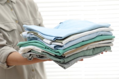 Photo of Woman with stack of clean clothes indoors, closeup