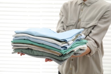 Photo of Woman with stack of clean clothes indoors, closeup