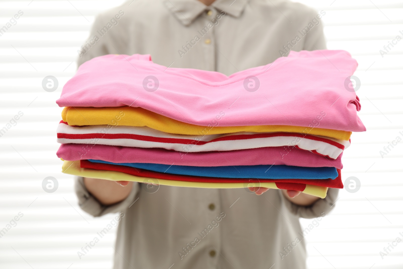 Photo of Woman with stack of clean clothes indoors, closeup