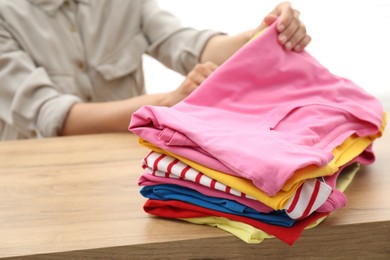 Woman stacking clean clothes at wooden table indoors, closeup