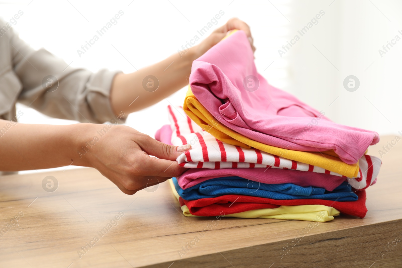 Photo of Woman stacking clean clothes at wooden table indoors, closeup