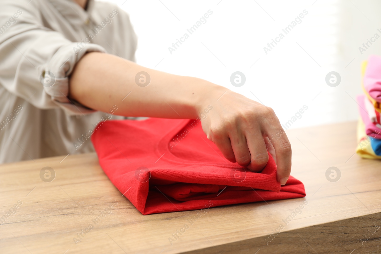 Photo of Woman stacking red shirt at wooden table indoors, closeup