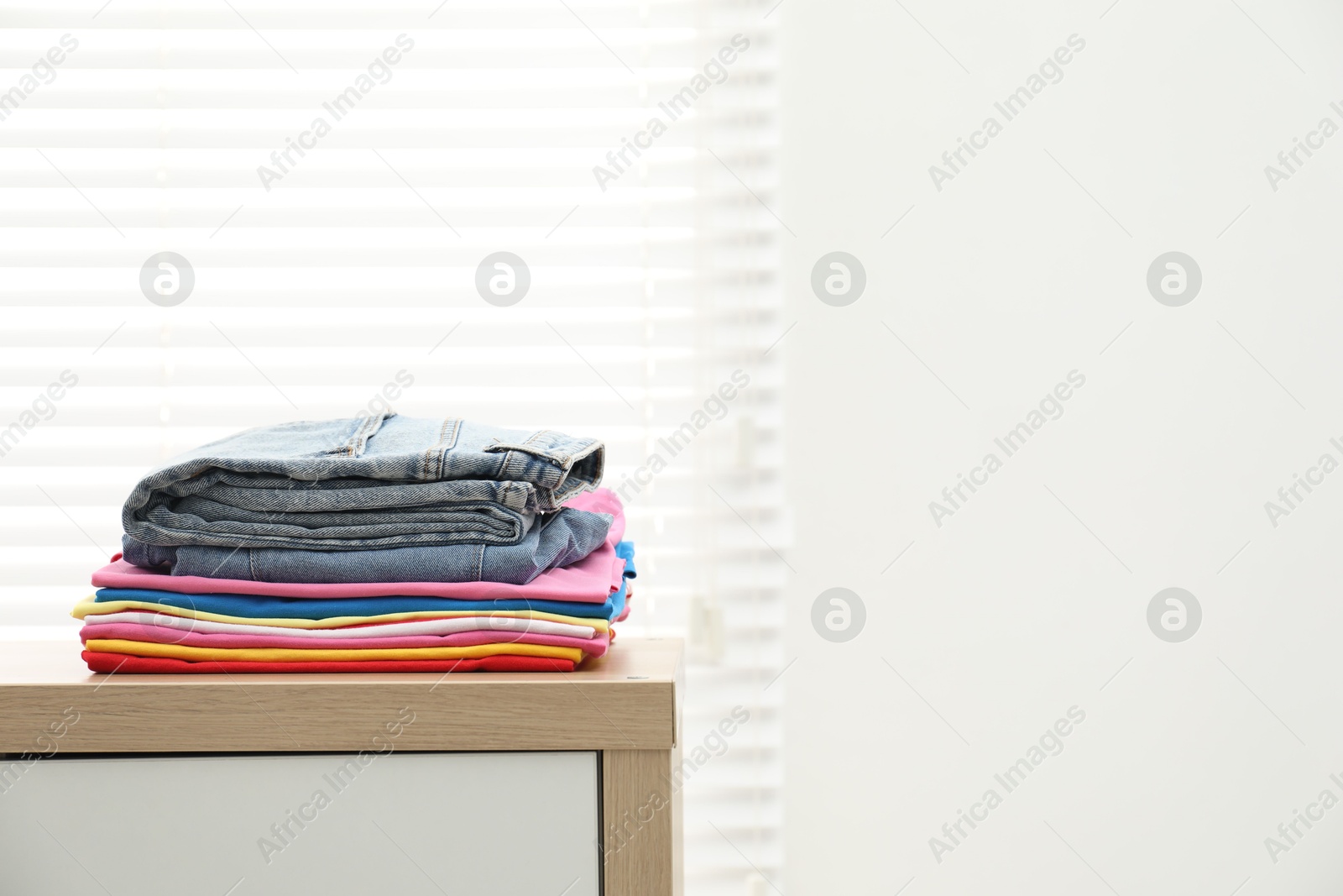 Photo of Stack of clean clothes on wooden dresser indoors, space for text