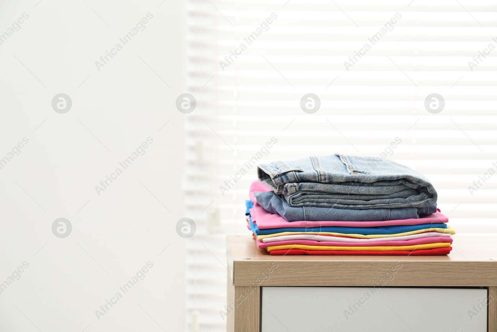 Photo of Stack of clean clothes on wooden dresser indoors, space for text