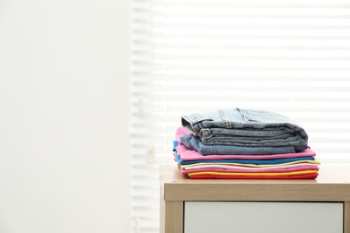 Photo of Stack of clean clothes on wooden dresser indoors, space for text