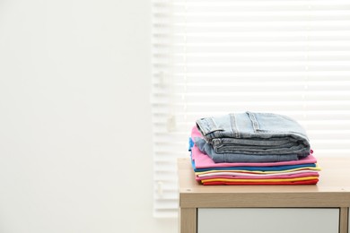 Photo of Stack of clean clothes on wooden dresser indoors, space for text