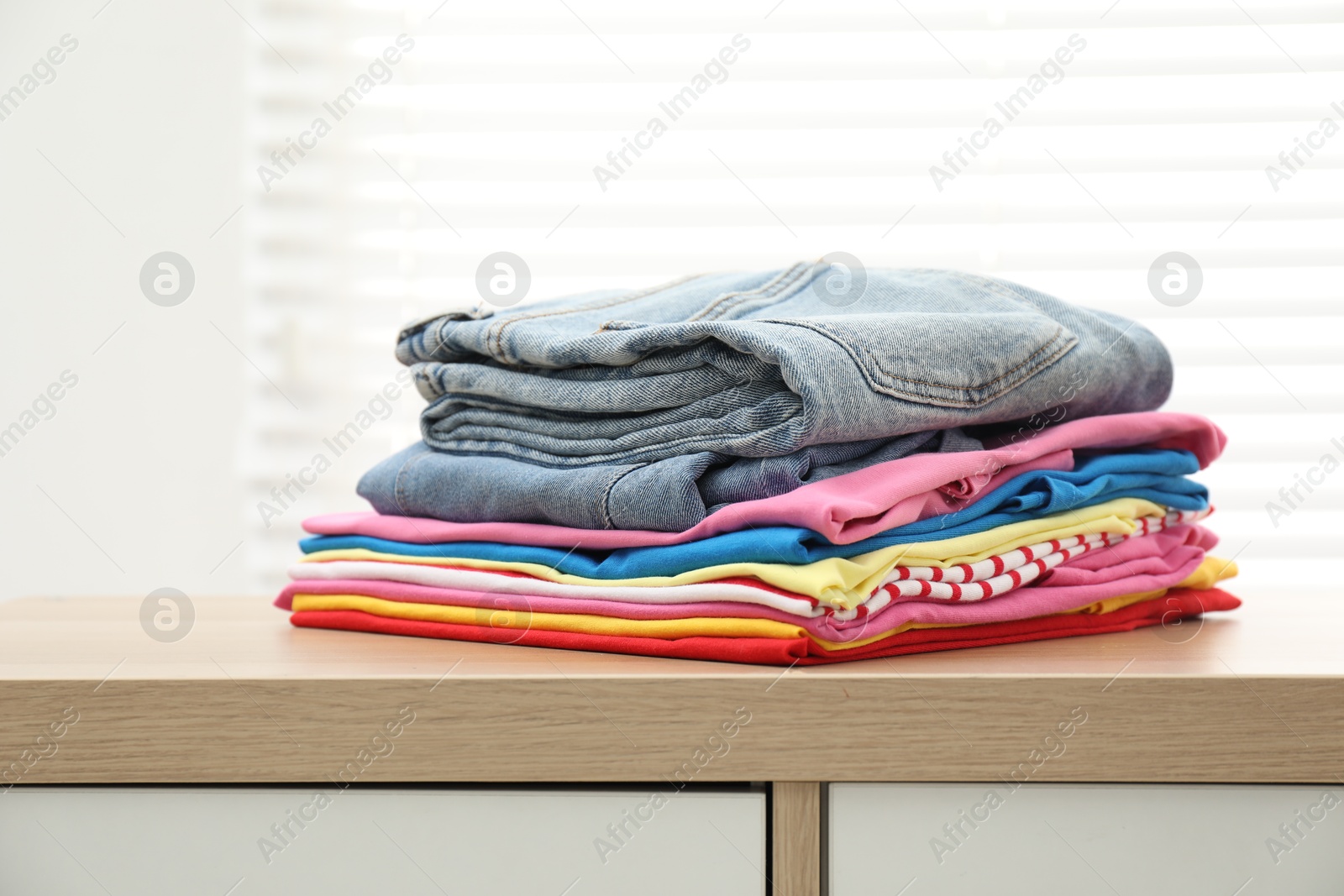 Photo of Stack of clean clothes on wooden dresser indoors