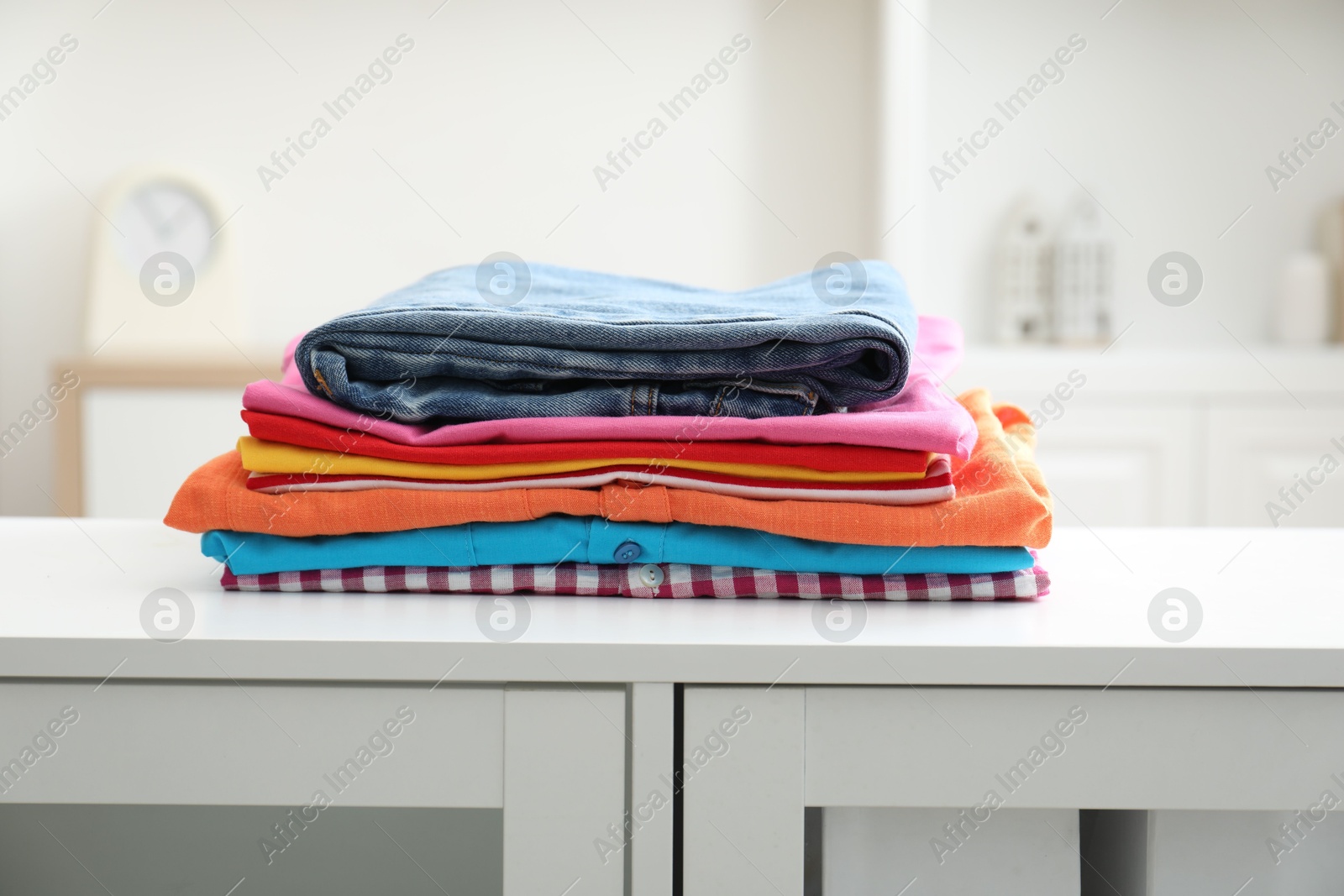 Photo of Stack of clean clothes on white dresser indoors