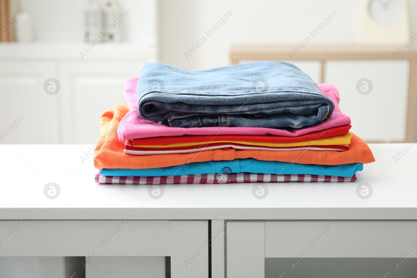 Photo of Stack of clean clothes on white dresser indoors