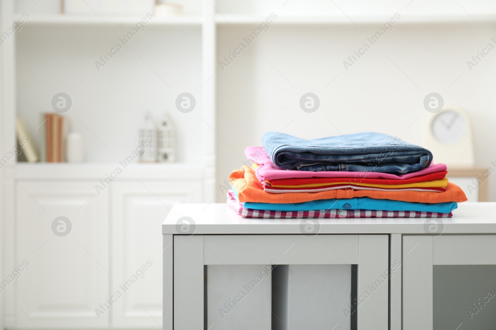 Photo of Stack of clean clothes on white dresser indoors