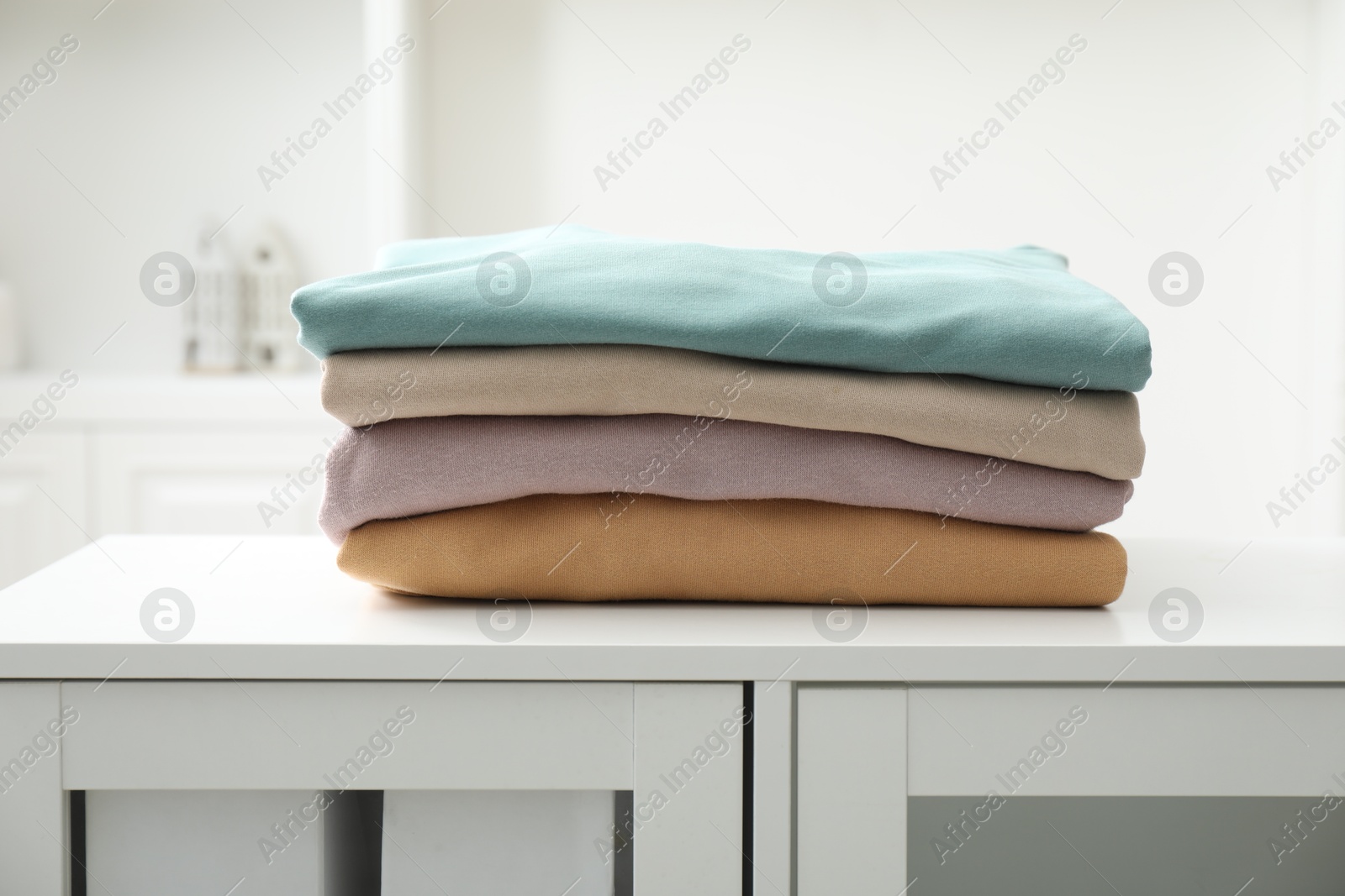 Photo of Stack of clean clothes on white dresser indoors