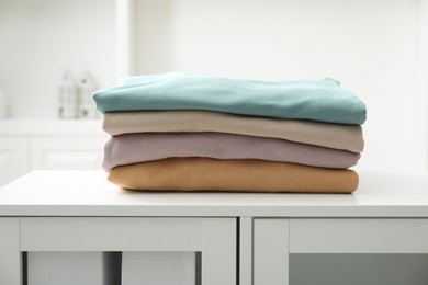 Photo of Stack of clean clothes on white dresser indoors