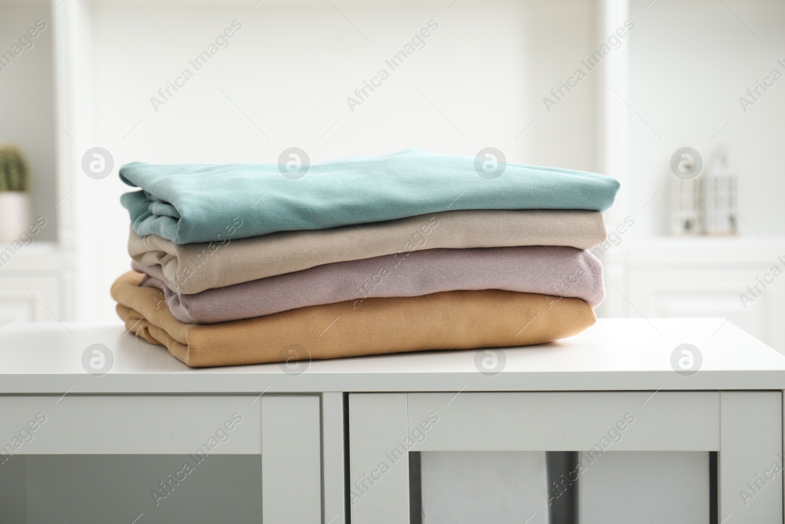 Photo of Stack of clean clothes on white dresser indoors