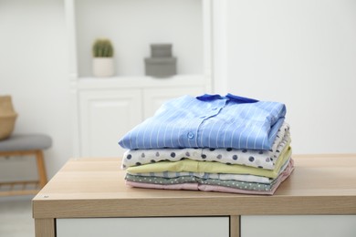 Photo of Stack of clean clothes on wooden dresser indoors