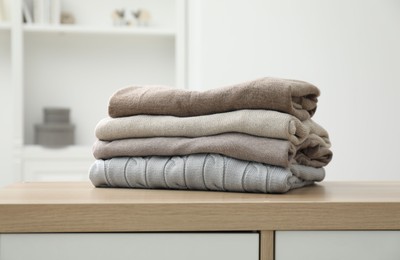 Photo of Stack of clean clothes on wooden dresser indoors