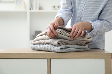 Photo of Woman stacking clean clothes at wooden dresser indoors, closeup