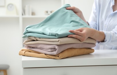 Woman stacking clean clothes at white table indoors, closeup