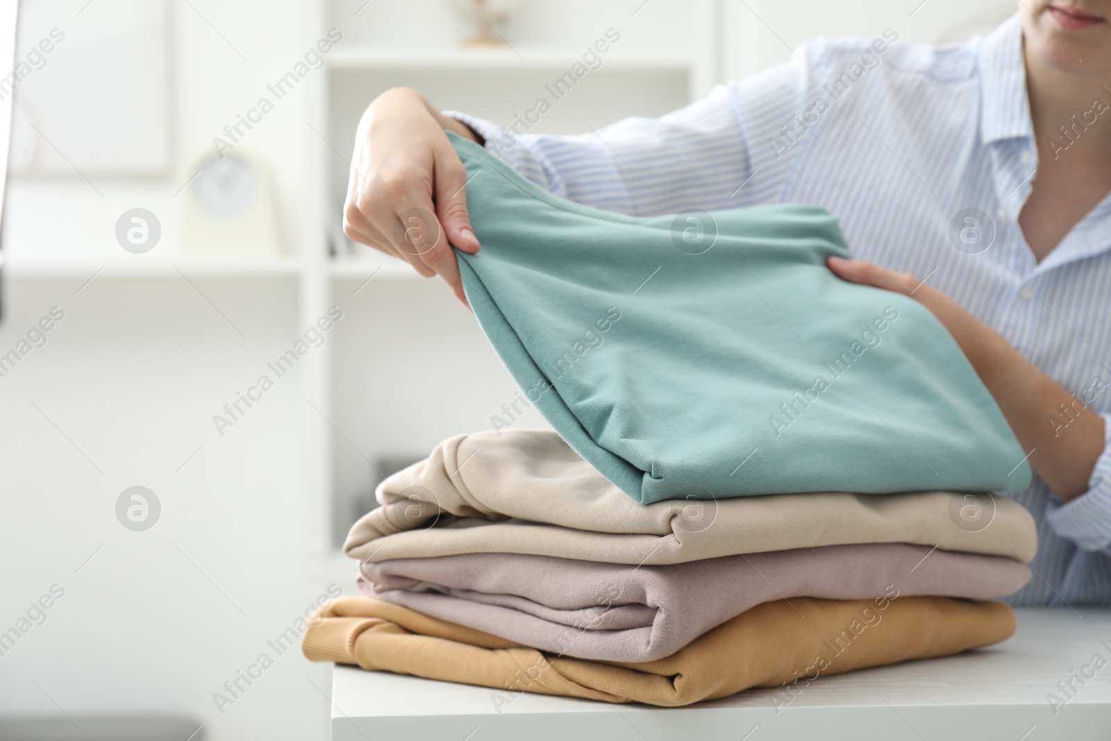 Photo of Woman stacking clean clothes at white table indoors, closeup