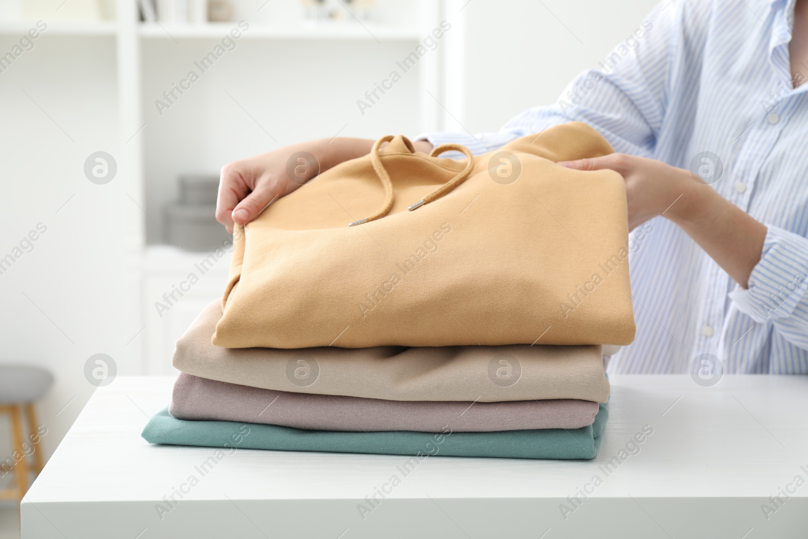 Photo of Woman stacking clean clothes at white table indoors, closeup