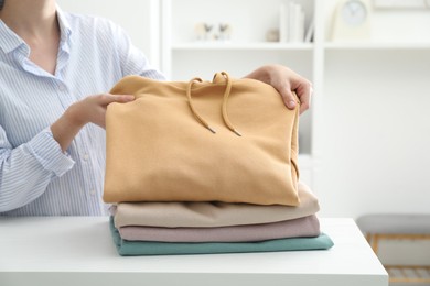 Woman stacking clean clothes at white table indoors, closeup