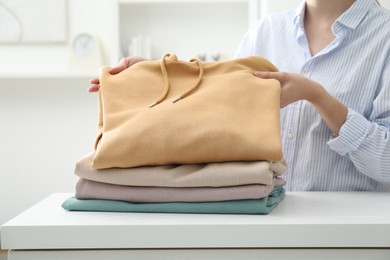 Photo of Woman stacking clean clothes at white table indoors, closeup