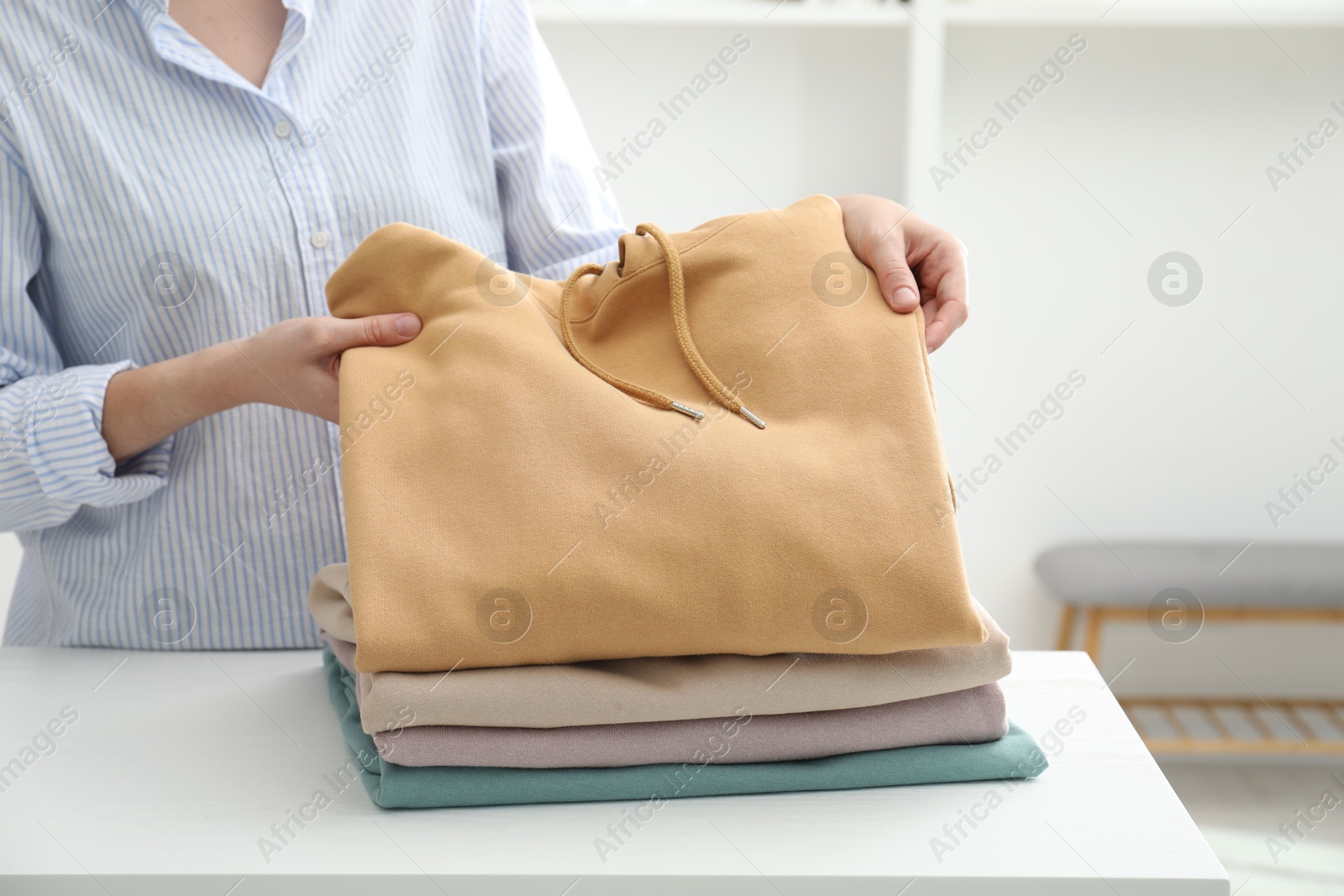 Photo of Woman stacking clean clothes at white table indoors, closeup