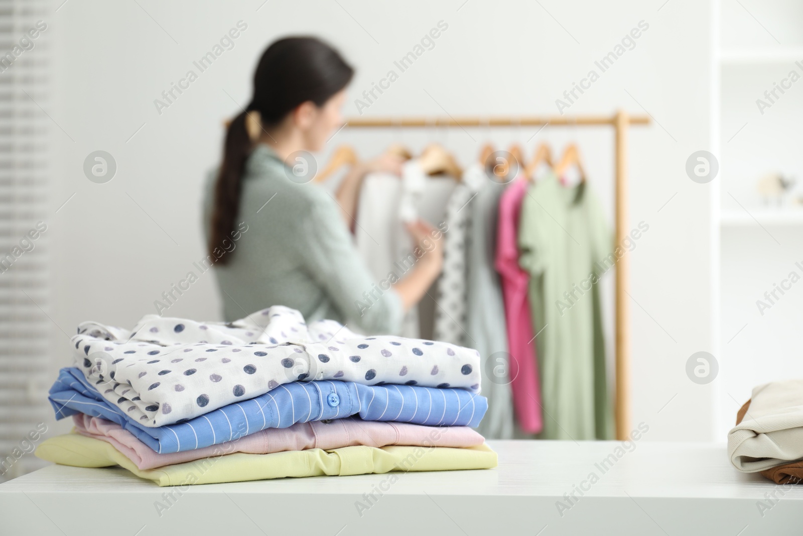 Photo of Woman choosing outfit near rack indoors, focus on stack of clothes