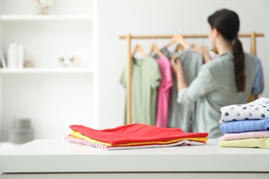 Photo of Woman choosing outfit near rack indoors, focus on stacks of clothes