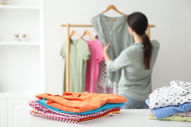 Woman choosing outfit near rack indoors, focus on stacks of clothes