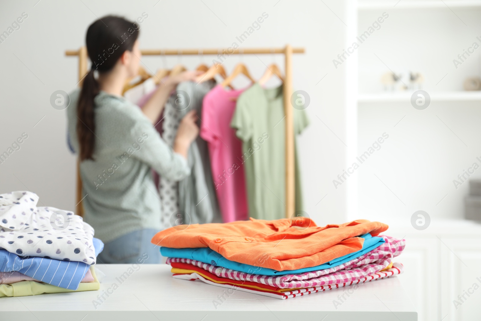 Photo of Woman choosing outfit near rack indoors, focus on stacks of clothes