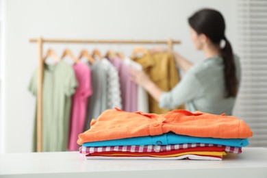 Photo of Woman choosing outfit near rack indoors, focus on stack of clothes