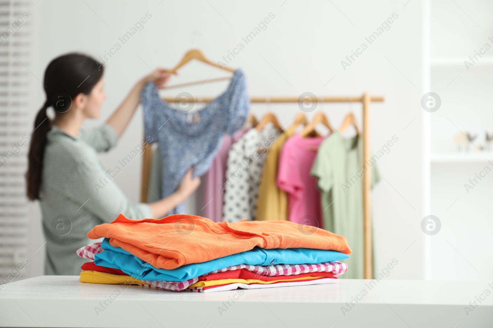 Photo of Woman choosing outfit near rack indoors, focus on stack of clothes