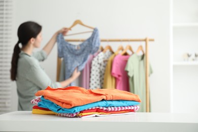 Woman choosing outfit near rack indoors, focus on stack of clothes