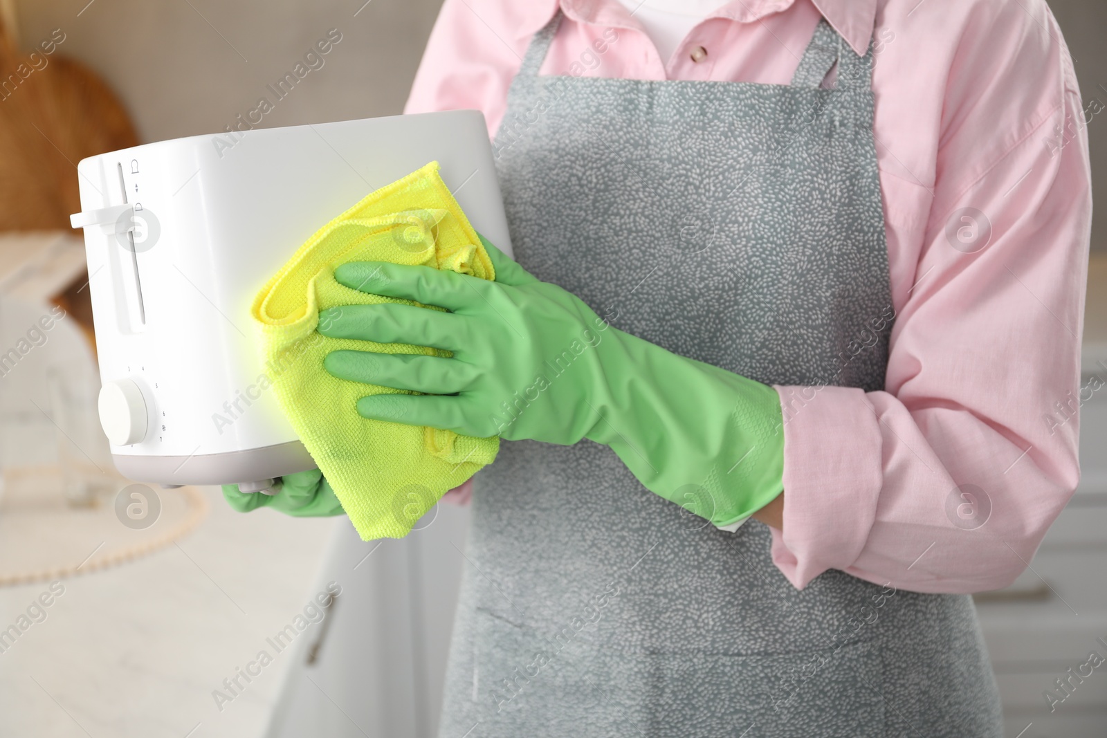 Photo of Woman wiping toaster with rag in kitchen, closeup