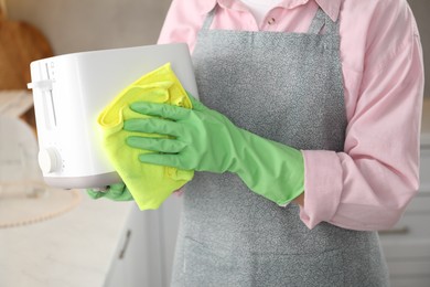 Photo of Woman wiping toaster with rag in kitchen, closeup