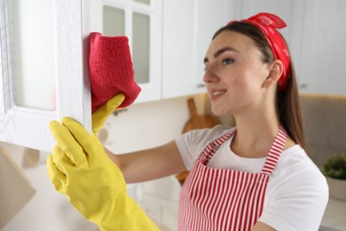 Photo of Beautiful young woman cleaning furniture with rag in kitchen, selective focus