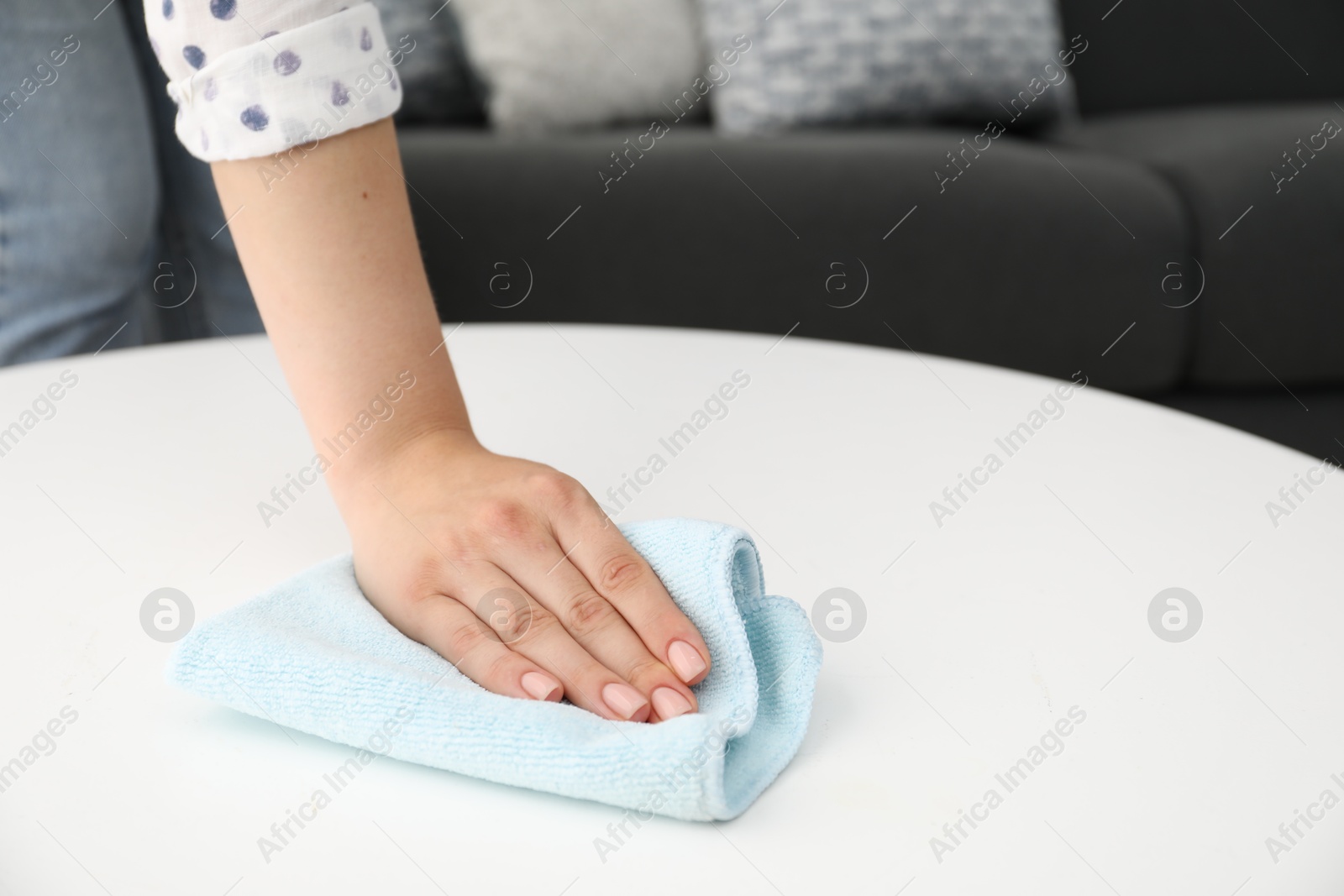 Photo of Woman wiping coffee table with rag indoors, closeup