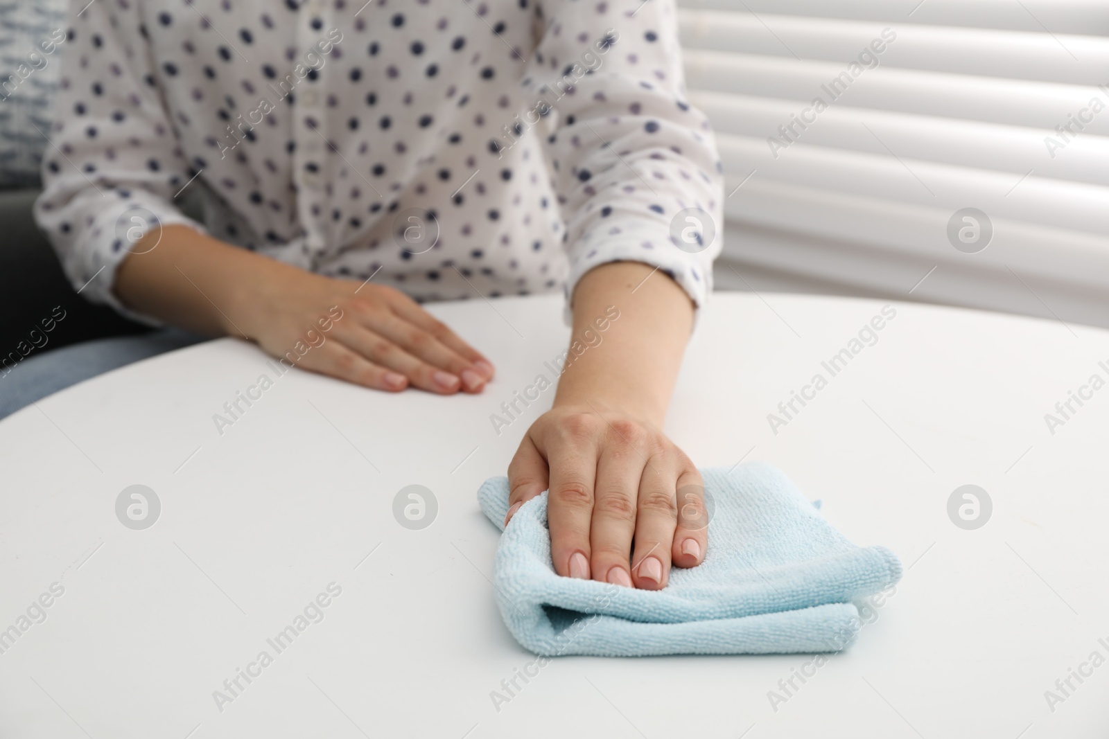 Photo of Woman wiping coffee table with rag indoors, closeup