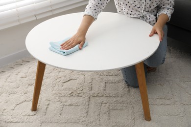 Photo of Woman wiping coffee table with rag indoors, closeup