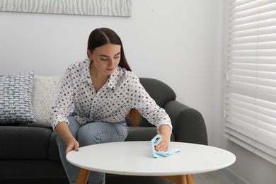 Beautiful young woman wiping coffee table with rag at home