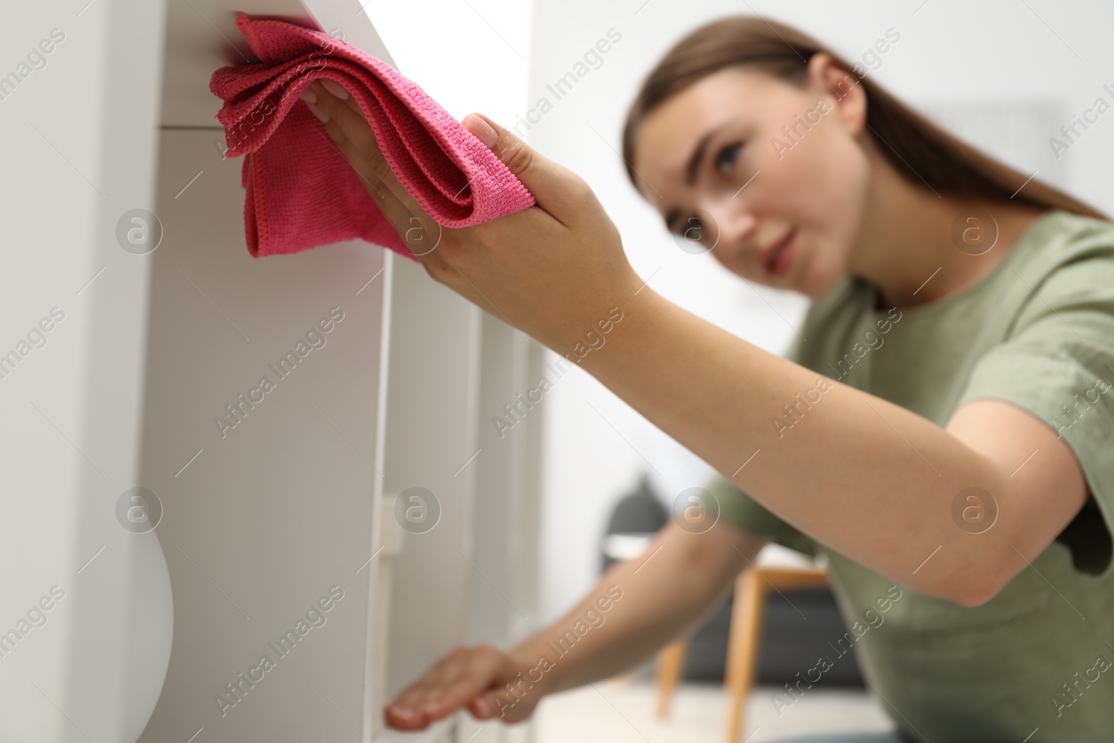 Photo of Beautiful young woman wiping furniture with rag indoors, selective focus