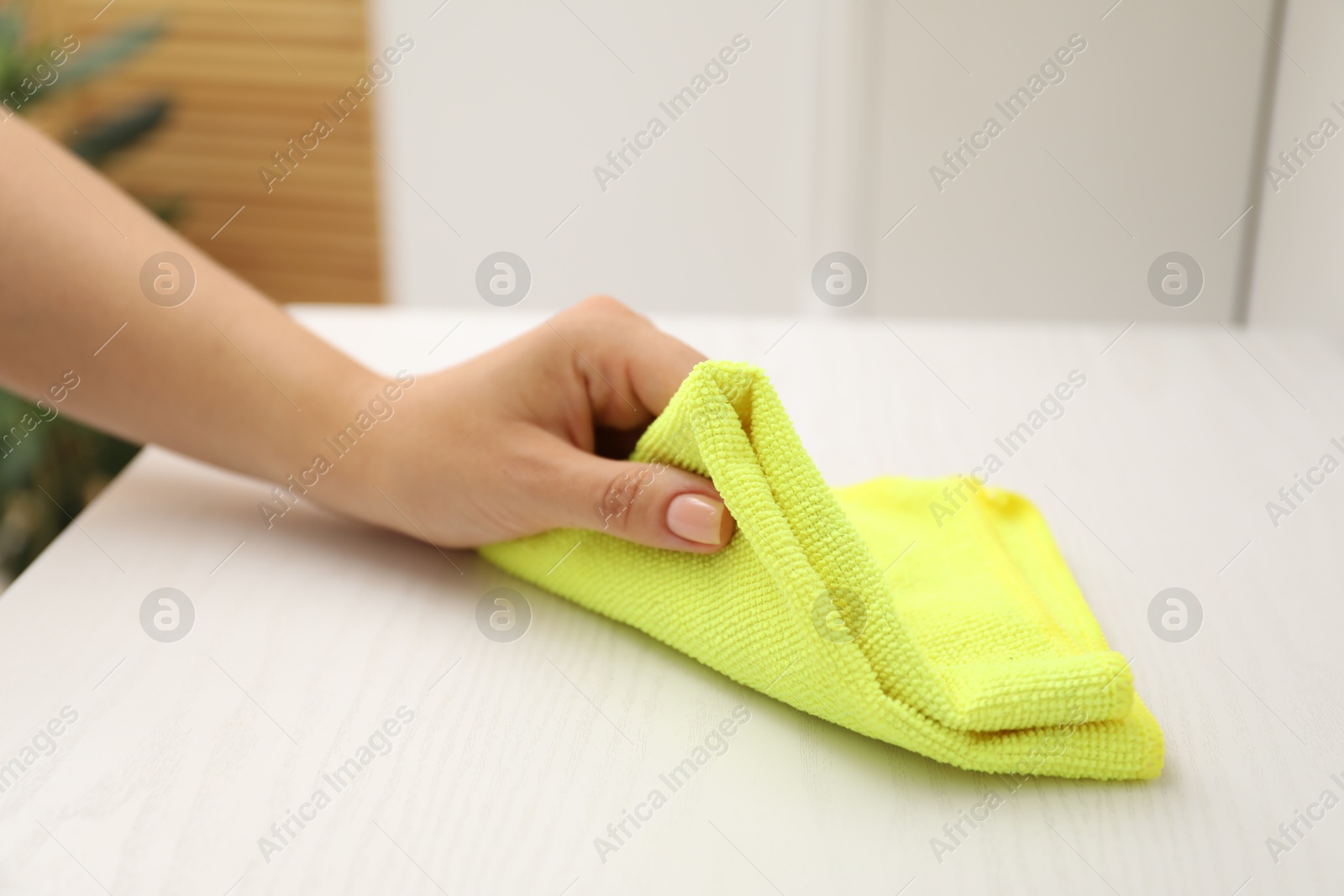 Photo of Woman wiping white table with rag indoors, closeup