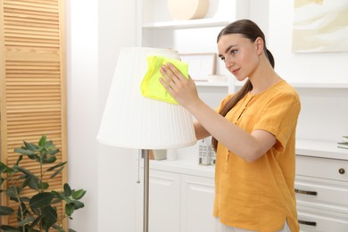 Photo of Beautiful young woman cleaning floor lamp with rag at home