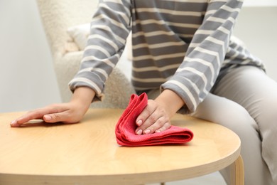 Woman wiping coffee table with rag indoors, closeup